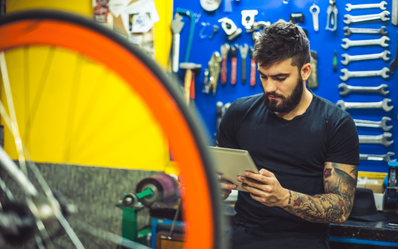 Small business bike repair shop owner looking at tablet wondering if accounting is worth it