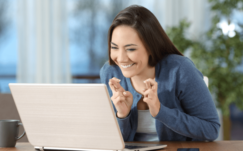 Small business owner crossing fingers looking excited at laptop computer to see if she is eligible for the ERC
